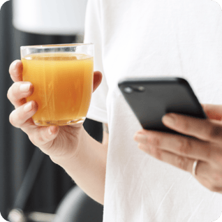 a person holding a smartphone and a glass of orange juice