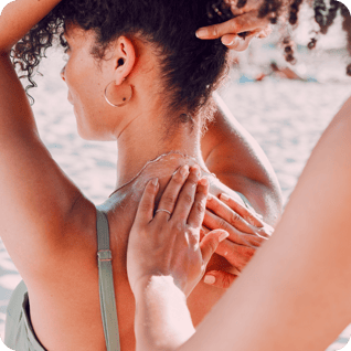 a woman at the beach getting suncream applied to her back 