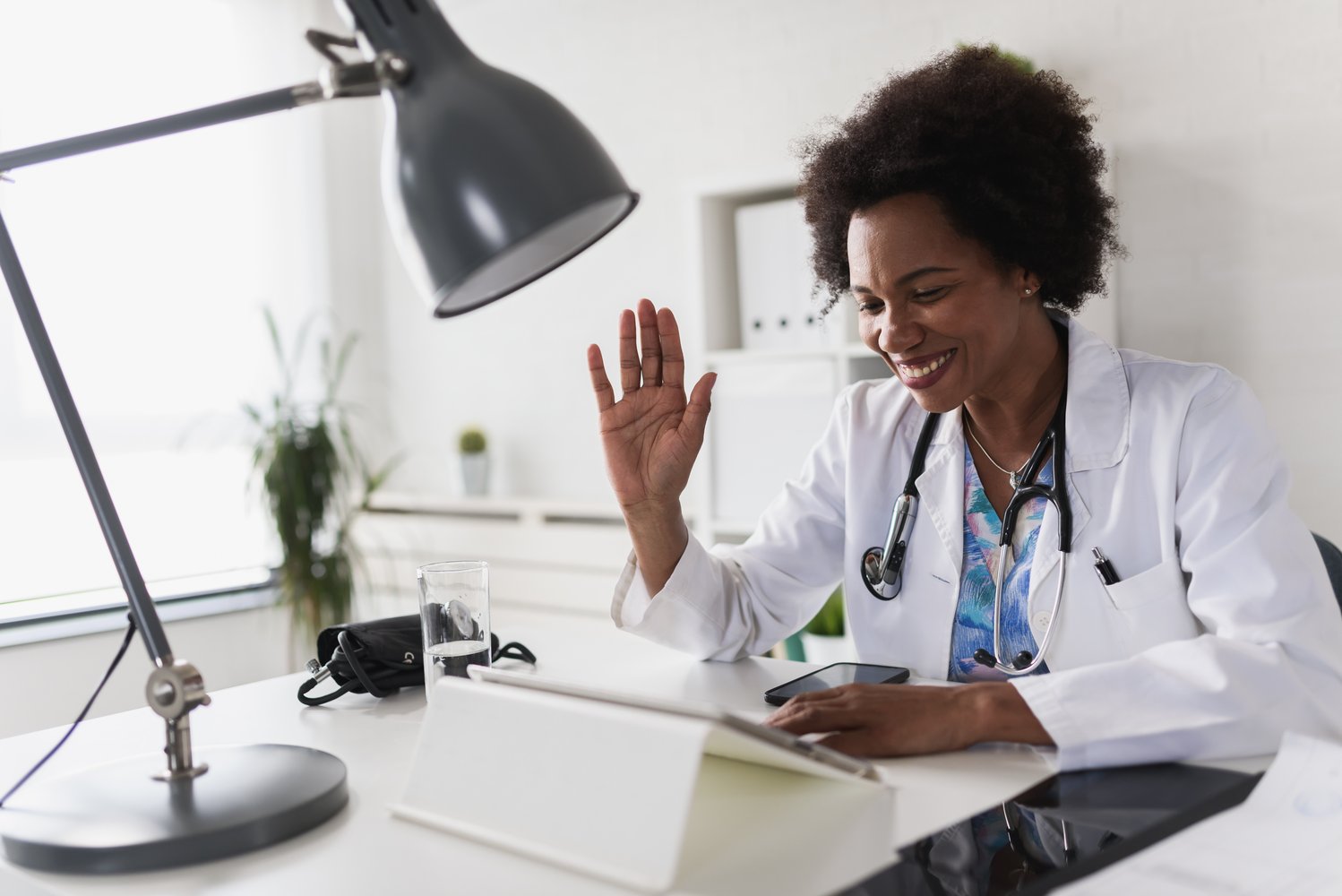 Female GP waving at patient on her computer