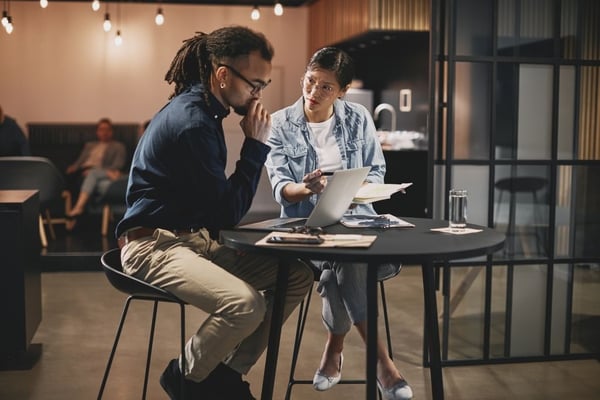 Image shows two people sitting at a table looking at a laptop